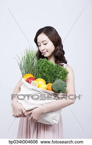 Stock Photograph - A woman in dress looking at a bag of vegetables in her arms. Fotosearch
