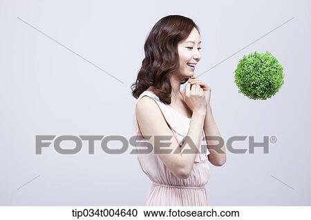 Stock Image - A woman in dress smiling at a ball made from grass floating in the air. Fotosearch