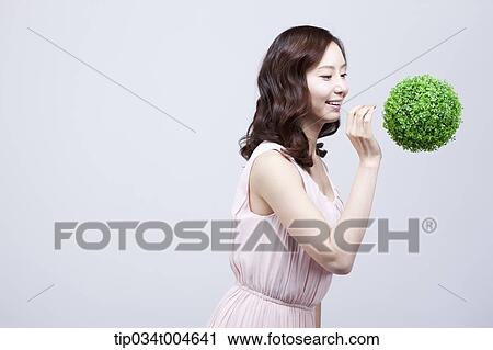 Stock Image - A woman in dress smiling at a ball made from grass floating in the air. Fotosearch