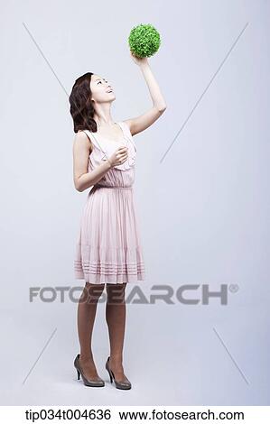 Stock Photograph - A woman in dress touching a ball made from grass. Fotosearch
