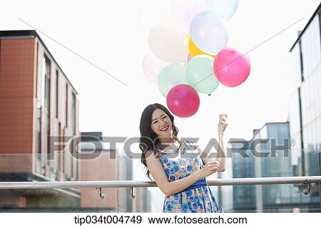 a woman in flower printed outfit posing with a bunch of balloons in a building balcony View Large Photo Image Stock Photo - a woman in flower printed outfit posing with a bunch of balloons in a building balcony. Fotosearch