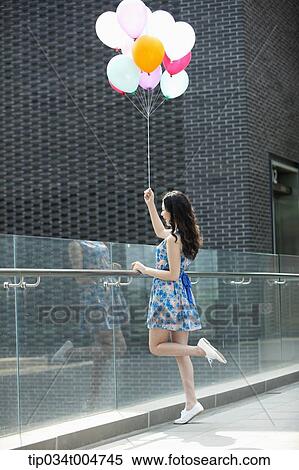 Stock Photography - a woman in flower printed outfit posing with a bunch of balloons in a building balcony. Fotosearch