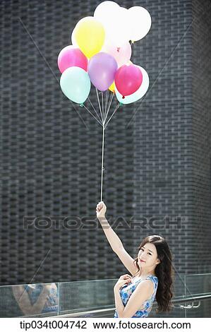 a woman in flower printed outfit holding a bunch of balloons in a building balcony View Large Photo Image Stock Image - a woman in flower printed outfit holding a bunch of balloons in a building balcony. Fotosearch