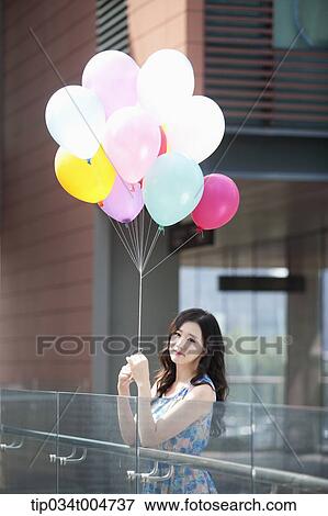 a woman in flower printed outfit holding a bunch of balloons in a building balcony View Large Photo Image Stock Photo - a woman in flower printed outfit holding a bunch of balloons in a building balcony. Fotosearch