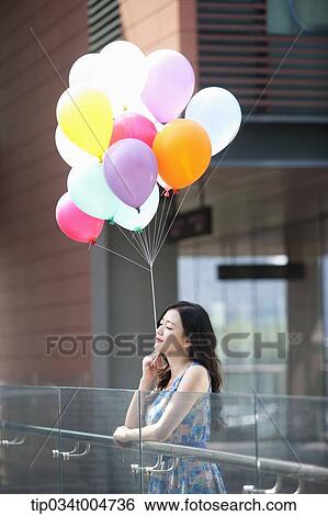 a woman in flower printed outfit holding a bunch of balloons in a building balcony View Large Photo Image Stock Photograph - a woman in flower printed outfit holding a bunch of balloons in a building balcony. Fotosearch
