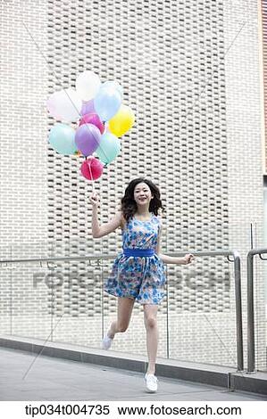 Stock Photography - a woman in flower printed outfit running with a bunch of balloons. Fotosearch