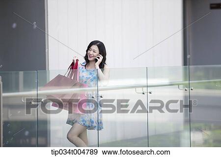 a woman in flower printed outfit with shopping bags talking on a mobile phone View Large Photo Image Stock Photo - a woman in flower printed outfit with shopping bags talking on a mobile phone. Fotosearch