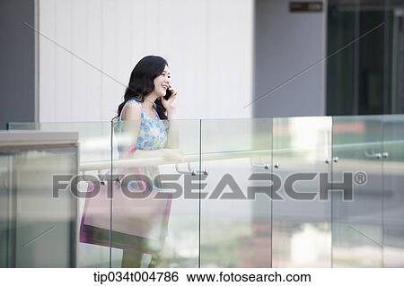 Stock Photograph - a woman in flower printed outfit with shopping bags talking on a mobile phone. Fotosearch