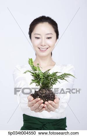 Stock Image - a woman in green skirt giving a plant with roots. Fotosearch