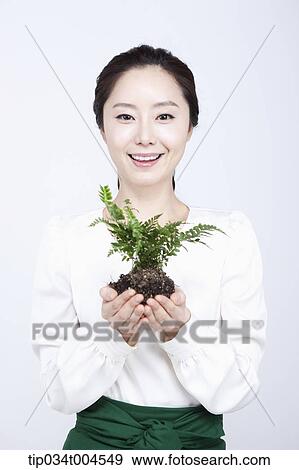 Stock Photo - a woman in green skirt holding a plant with roots. Fotosearch