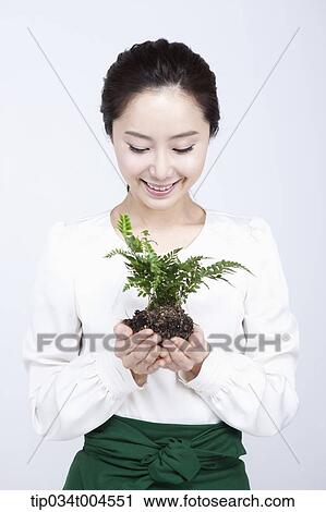Stock Image - a woman in green skirt looking at a plant with roots in her hands. Fotosearch