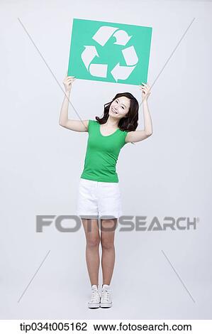 Stock Image - a woman in green t-shirt holding a recycling logo signboard . Fotosearch