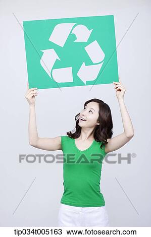 Stock Image - a woman in green t-shirt looking up at her recycling logo signboard . Fotosearch