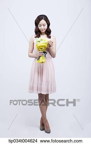 Picture - A woman looking at a flower bouquet in her hand. Fotosearch