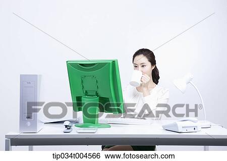 a woman sitting at office desk drinking a coffee View Large Photo Image Stock Photograph - a woman sitting at office desk drinking a coffee. Fotosearch