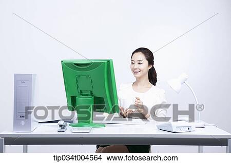Picture - a woman sitting at office desk holding a coffee cup. Fotosearch