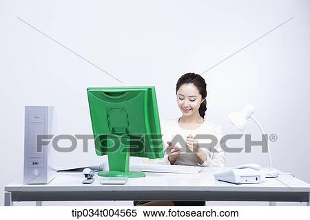 Stock Photography - a woman sitting at office desk holding a coffee cup. Fotosearch