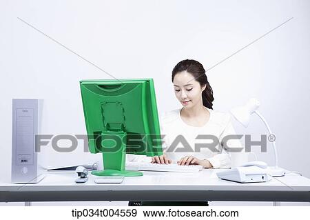 Stock Photo - a woman sitting at office desk typing. Fotosearch