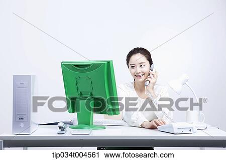 a woman sitting at office desk working making a call View Large Photo Image Stock Image - a woman sitting at office desk working making a call. Fotosearch