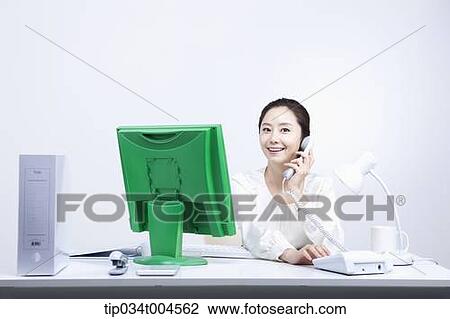 Stock Image - a woman sitting at office desk working making a call. Fotosearch