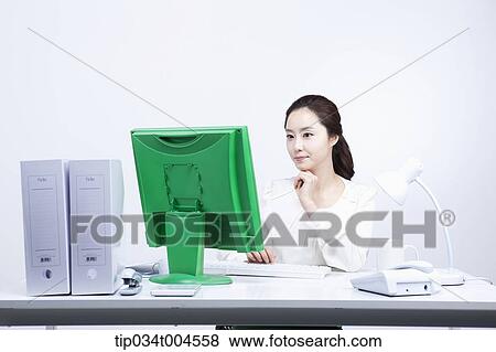 a woman sitting at office desk working with green computer View Large Photo Image Stock Photo - a woman sitting at office desk working with green computer. Fotosearch