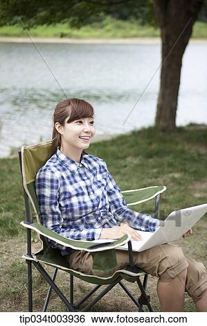 Stock Photograph - a woman sitting on a camping chair using laptop. Fotosearch