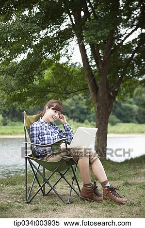 a woman sitting on a camping chair using laptop View Large Photo Image Stock Photography - a woman sitting on a camping chair using laptop. Fotosearch