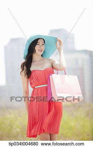 A woman smiling in coral dress and turquoise hat holding a shopping bag View Large Photo Image Stock Image - A woman smiling in coral dress and turquoise hat holding a shopping bag . Fotosearch