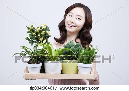 Stock Photo - A woman smiling while holding a tray of plants in different vases. Fotosearch