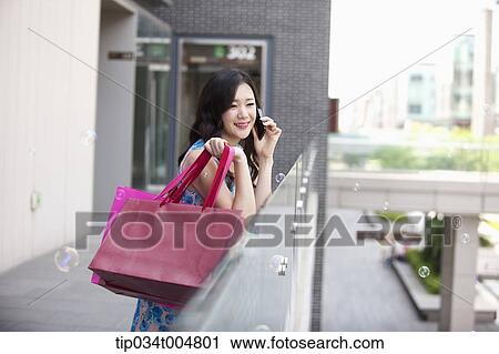 a woman smiling while holding shopping bags and a mobile phone View Large Photo Image Stock Image - a woman smiling while holding shopping bags and a mobile phone. Fotosearch