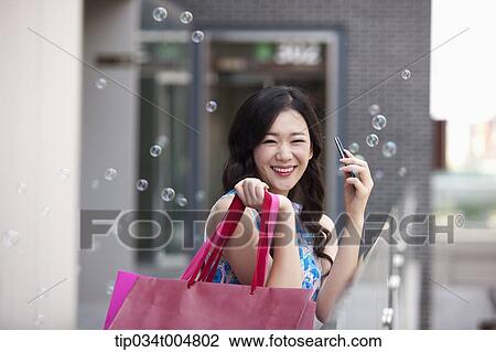 Stock Image - a woman smiling while holding shopping bags and a mobile phone. Fotosearch