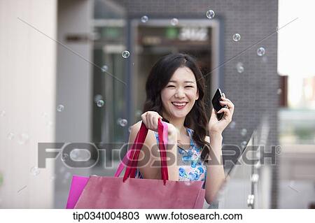 Stock Image - a woman smiling while holding shopping bags and a mobile phone. Fotosearch