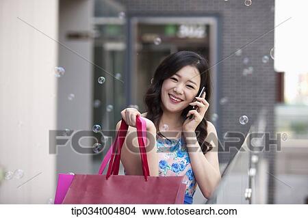 Picture - a woman smiling while talking on a mobile phone holding shopping bags . Fotosearch