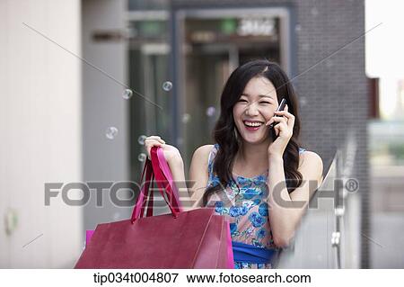 Stock Photo - a woman smiling while talking on a mobile phone holding shopping bags . Fotosearch