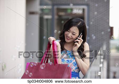 a woman smiling while talking on a mobile phone holding shopping bags View Large Photo Image Stock Photograph - a woman smiling while talking on a mobile phone holding shopping bags . Fotosearch