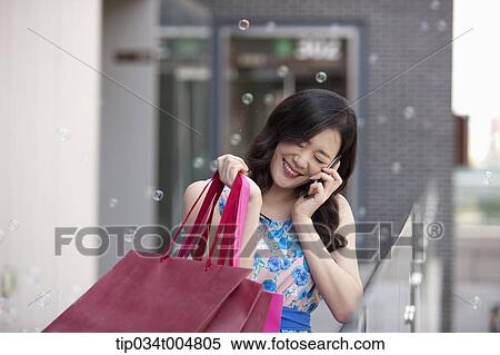 Stock Photography - a woman smiling while talking on a mobile phone holding shopping bags . Fotosearch