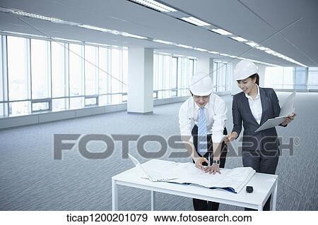 Stock Photo - architect executives discussing with blueprints on a desk of an empty room. Fotosearch