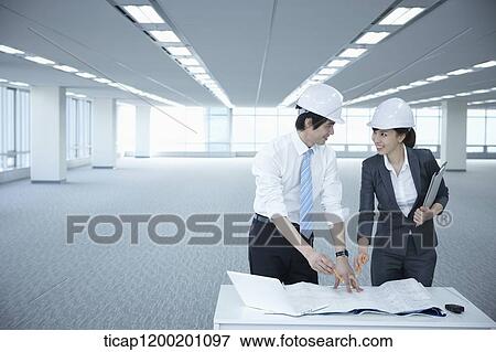 Stock Photo - architect executives discussing with blueprints on a desk of an empty room. Fotosearch