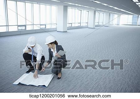 Stock Photograph - architect executives discussing with blueprints on the floor of an empty room . Fotosearch