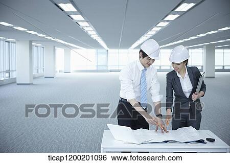 Stock Photograph - architect executives discussing with blueprints on a desk of an empty room. Fotosearch