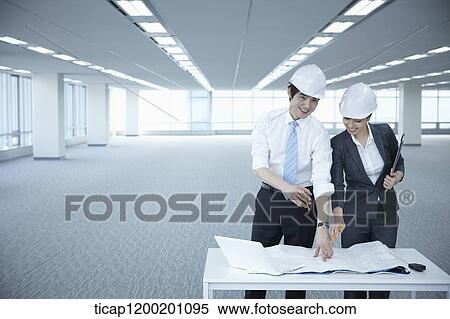 Stock Photography - architect executives discussing with blueprints on a desk of an empty room. Fotosearch
