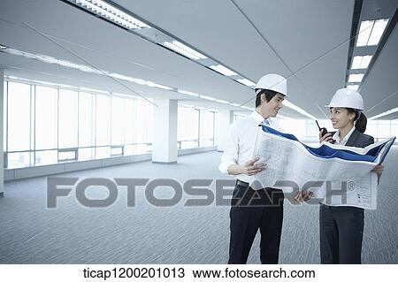 Stock Image - architect executives looking at blueprints in an empty room. Fotosearch