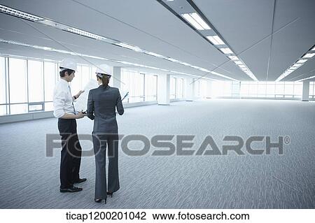 Stock Image - architect executives wearing construction helmets in an empty room . Fotosearch