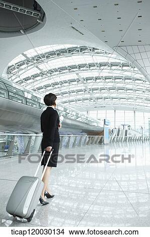 Picture - back of a businesswoman walking with luggage in Incheon airport. Fotosearch