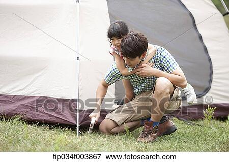 Stock Photo - daughter hugging from back of her father while he builds a tent. Fotosearch