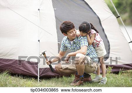 Stock Photography - daughter leaning on back of her father hammering to build a tent. Fotosearch