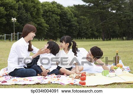 Stock Image - family having a picnic on a picnic blanket. Fotosearch