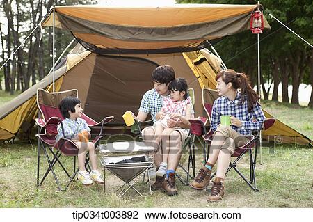 Stock Image - family sitting on camping chair talking while holding cups . Fotosearch