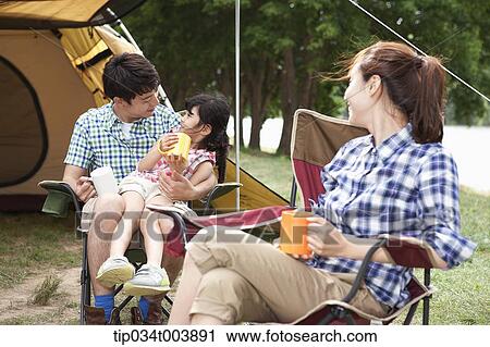 Stock Image - family talking while drinking while sat on camping chair. Fotosearch