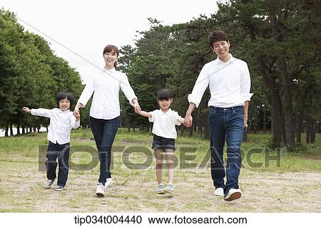 Stock Image - Family walking hand in hand on grass with trees behind. Fotosearch
